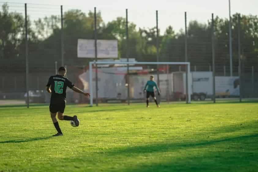 Jugador de espaldas chutando hacia la portería en un campo de fútbol
